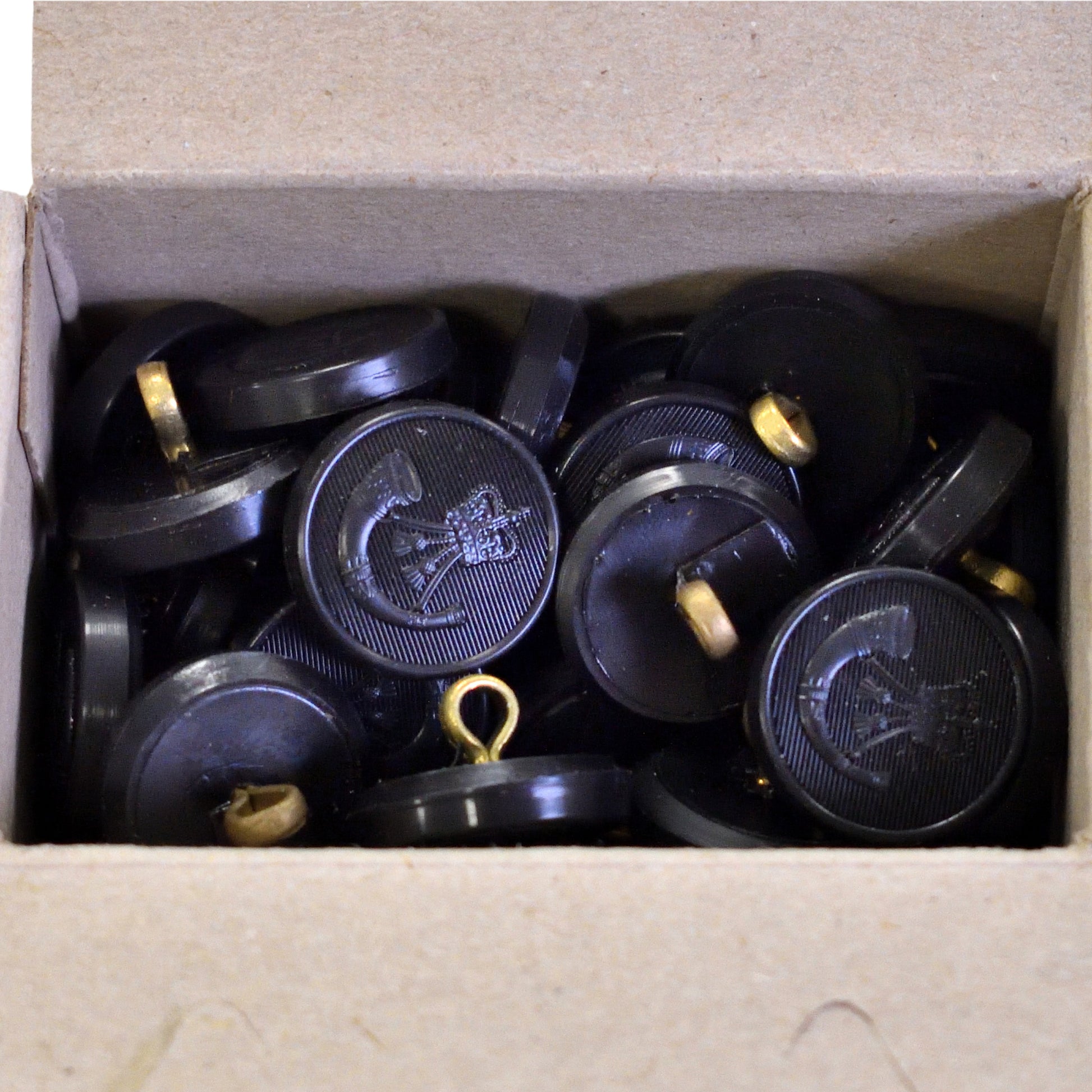 Top-down view of Firmin & Sons "The Rifles" black moulded buttons, box of 100.