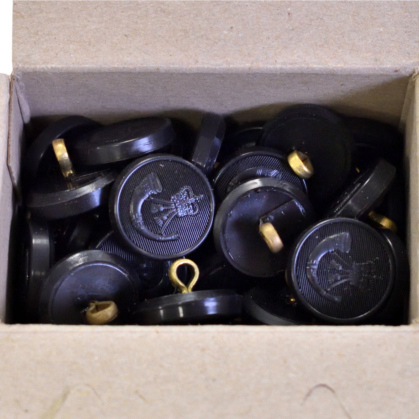 Top-down view of Firmin & Sons "The Rifles" black moulded buttons, box of 100.